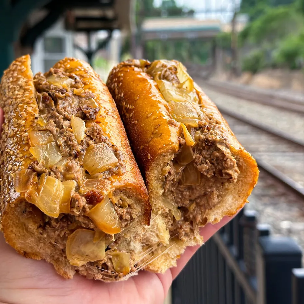 A Sum Pig cheesesteak held up beside the tracks at the Fort Washington Train Station